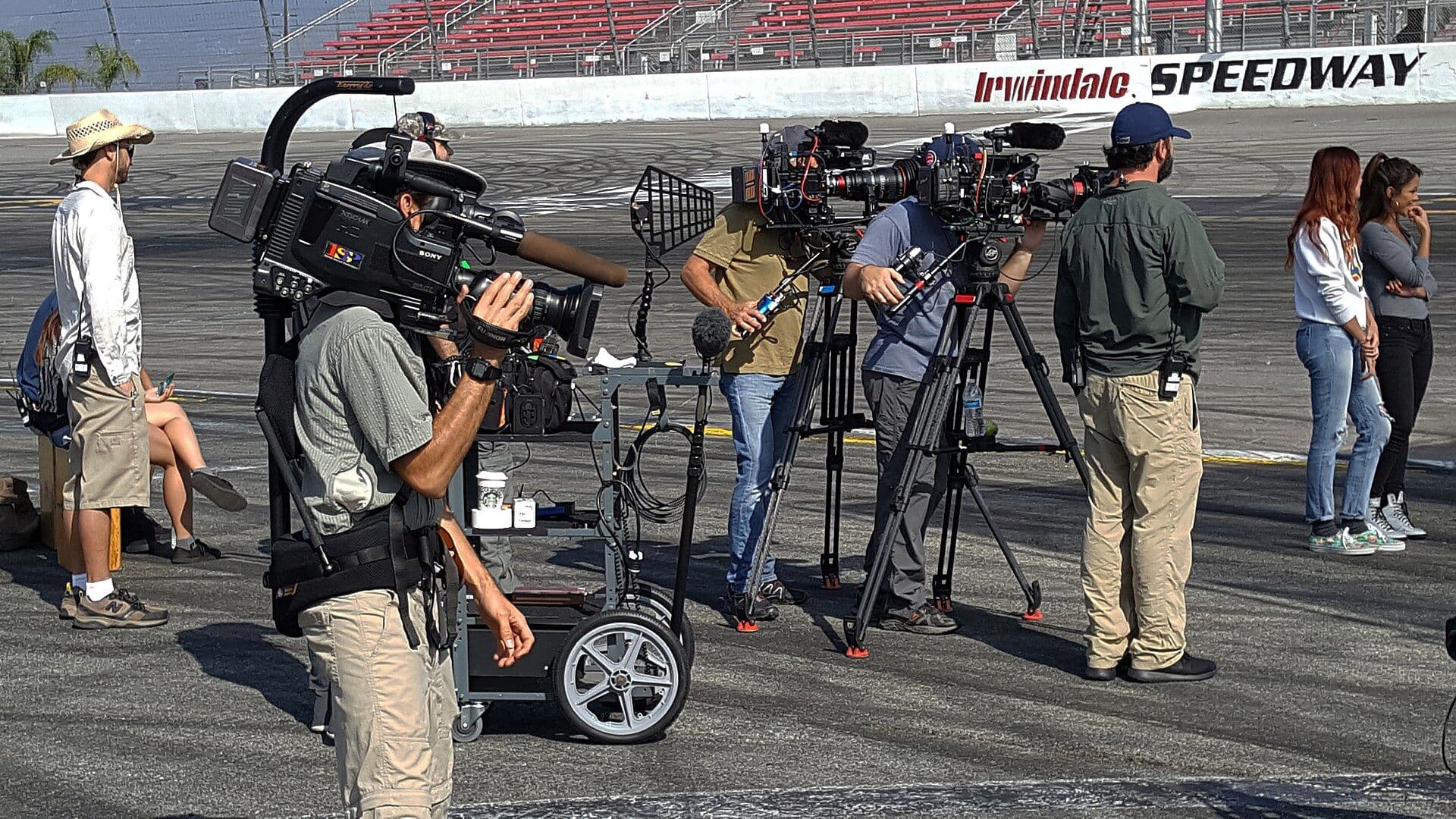 Production crew with camera and sound equipment filming at a speedway location