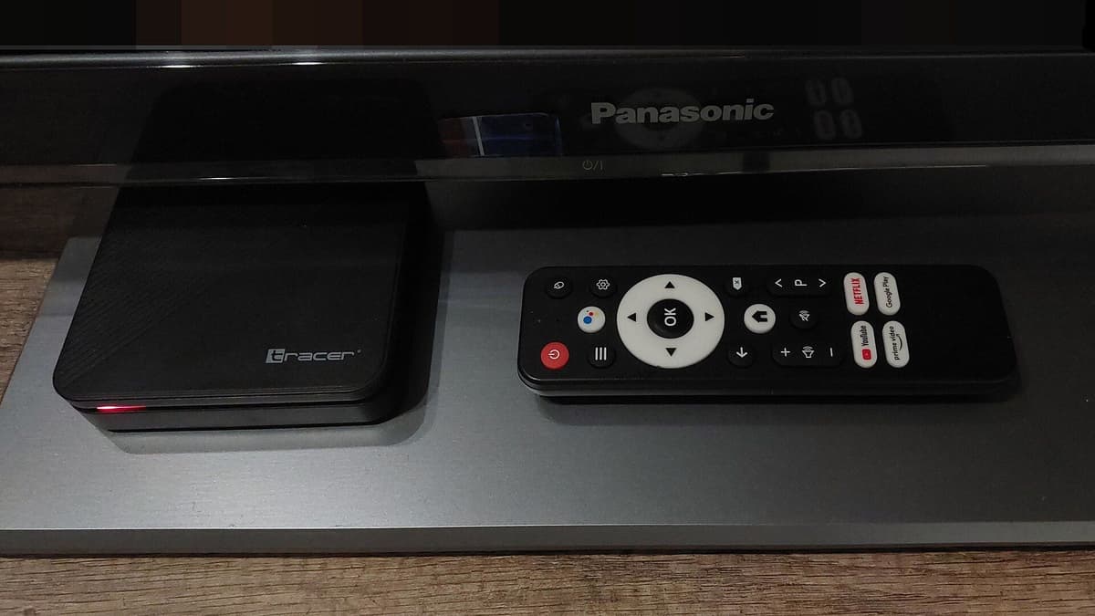 Black set-top box and a remote control on a shelf in front of a television