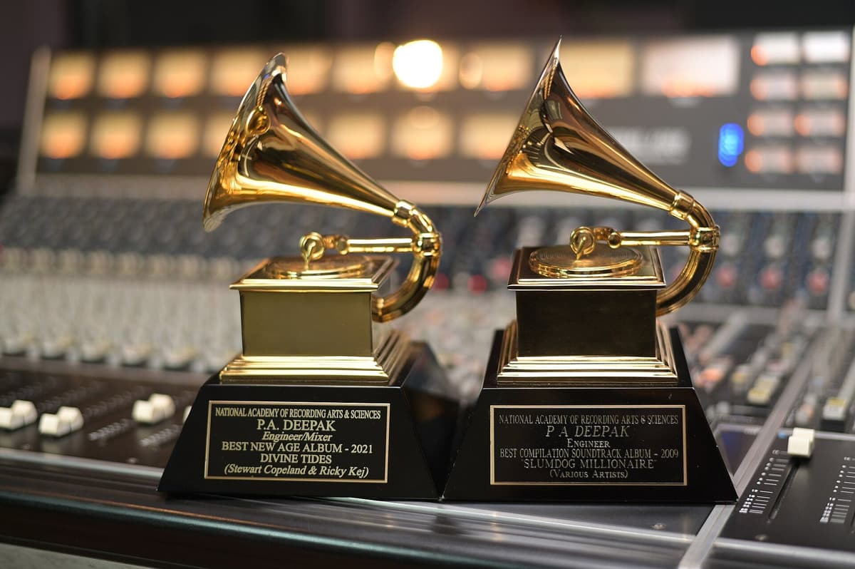 Two gold gramophone Grammy trophies on black bases with engraved plaques, resting on a studio mixing console