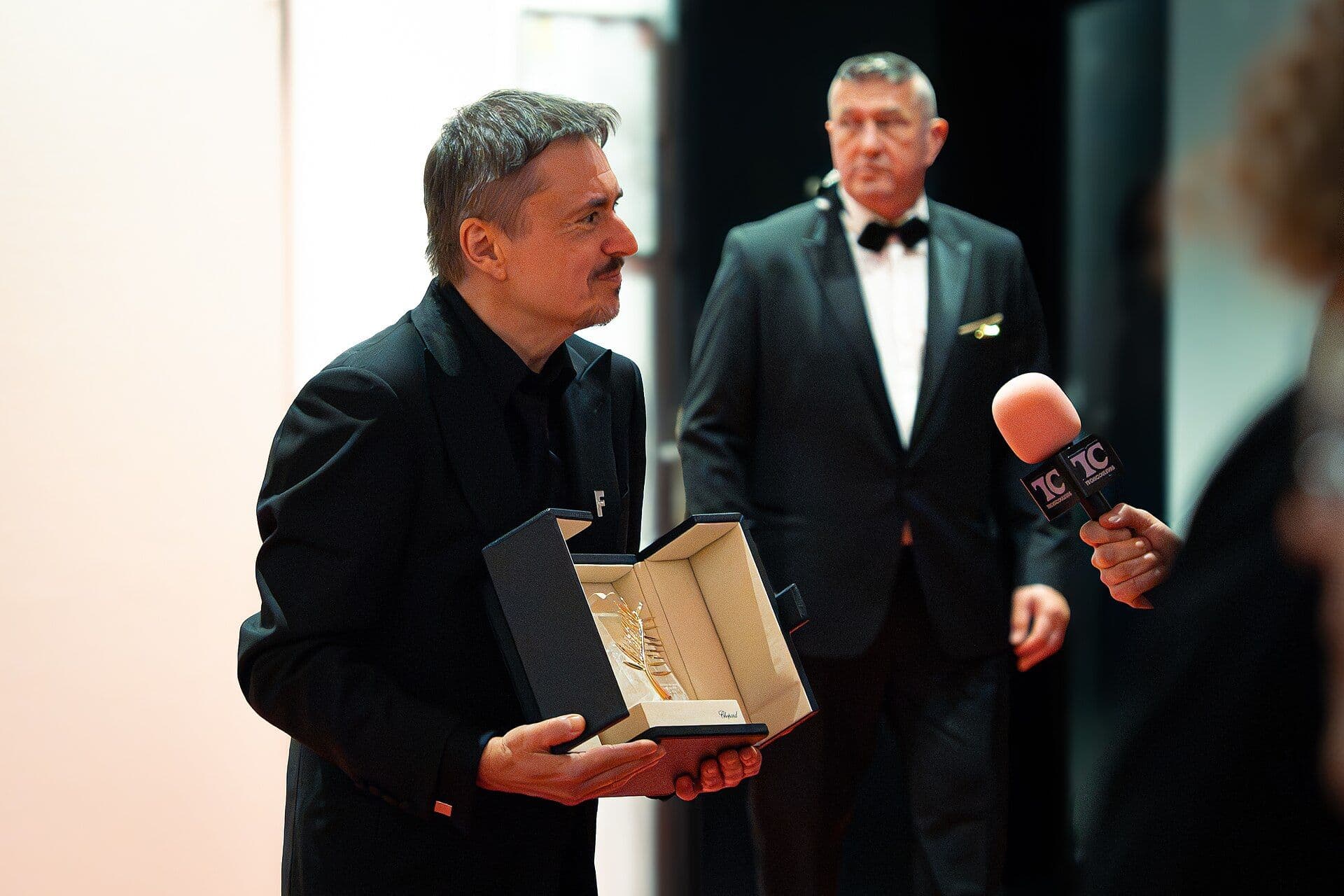A filmmaker holding the Palme d'Or award at a Cannes Film Festival press conference