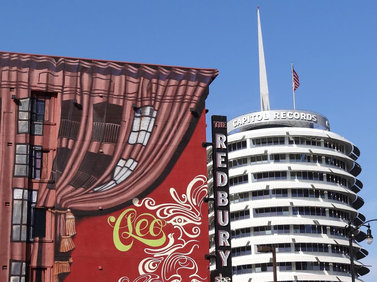 Capitol Records tower beside a red mural of a stage curtain and a vertical Redbury sign under a clear blue sky.