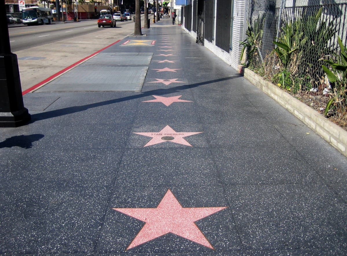 Pink terrazzo and brass stars of the Hollywood Walk of Fame embedded in the sidewalk with a red line visible