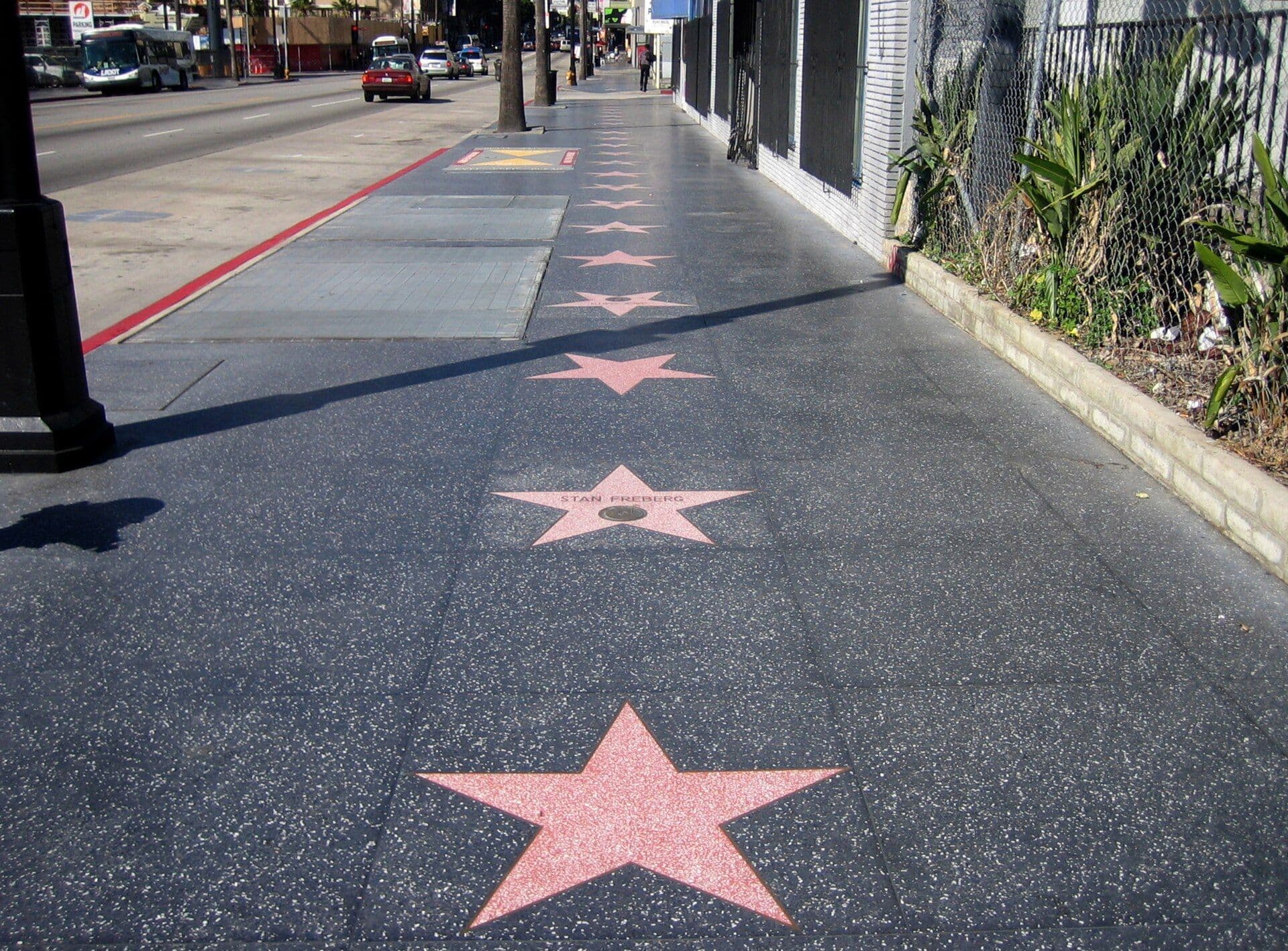 Pink terrazzo and brass stars of the Hollywood Walk of Fame embedded in the sidewalk with a red line visible