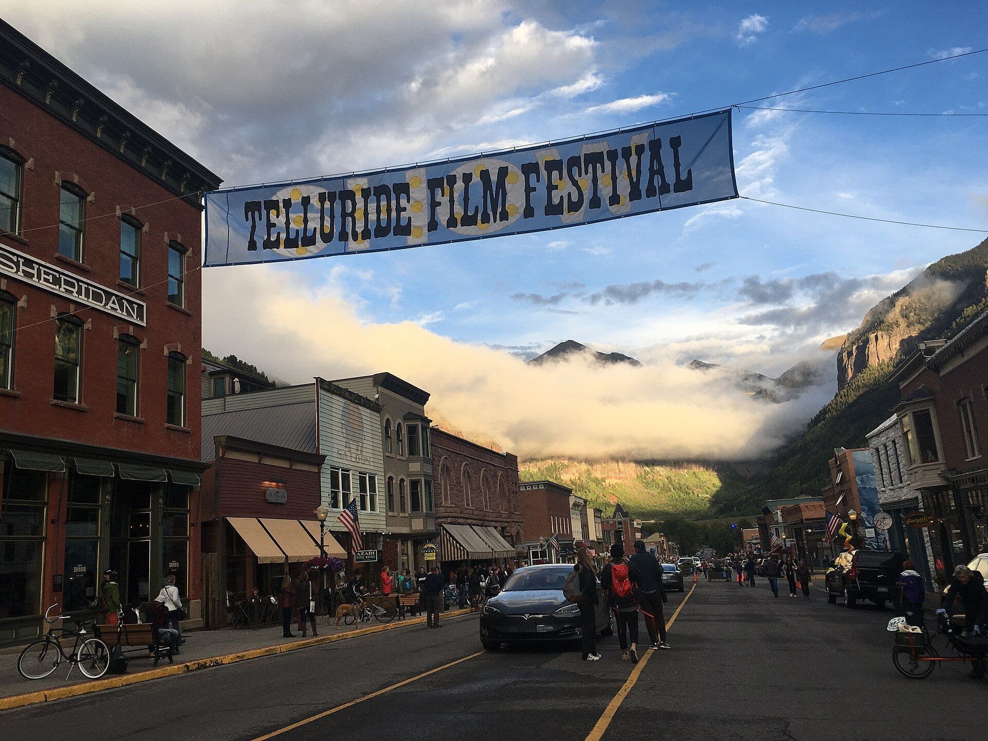 Telluride Film Festival banner stretches over Colorado Avenue as clouds drift through the mountains behind