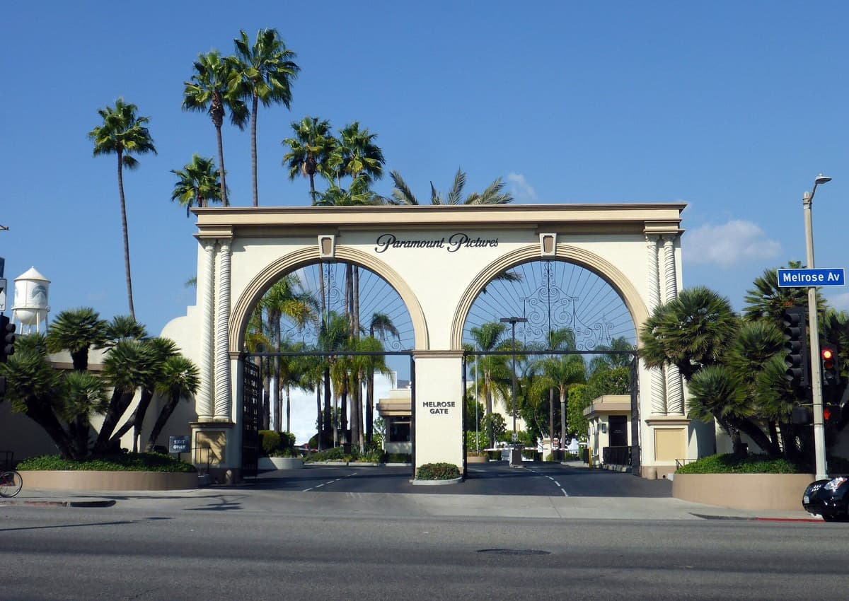 Arched Melrose Gate entrance with a Paramount Pictures sign, palm trees, and an empty street under blue sky.