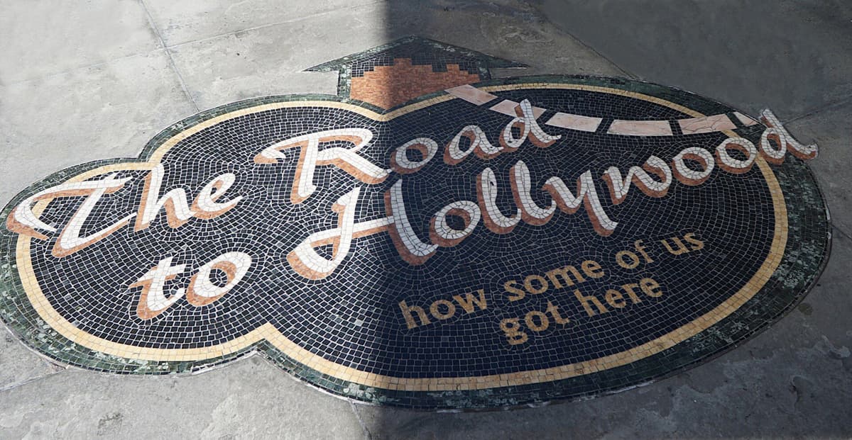 Mosaic floor sign reading 'The Road to Hollywood: how some of us got here' set in a grey paved surface