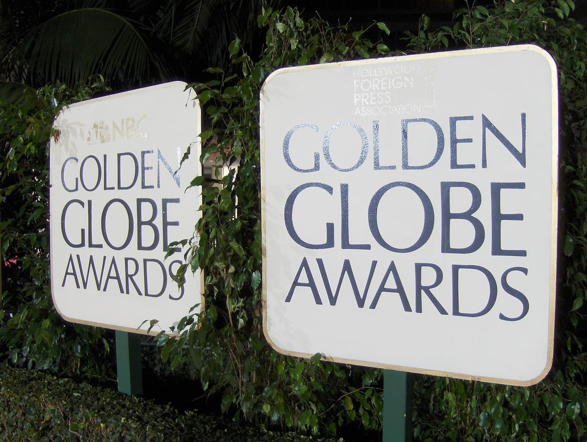 Two white Golden Globe Awards signs on green posts in front of ivy and dark palm foliage