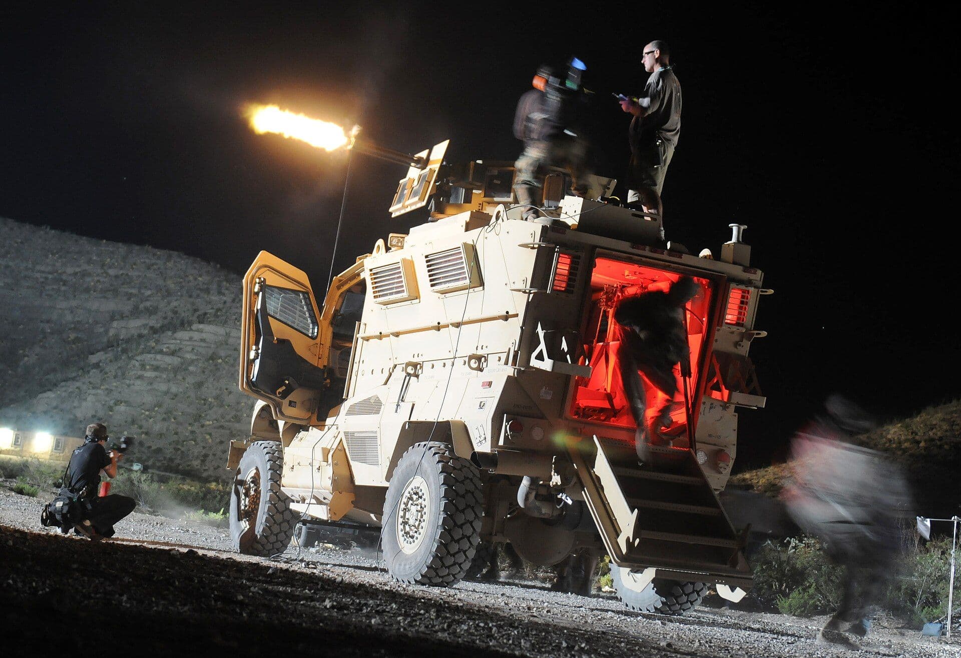 Production crew filming a nighttime scene with military vehicle and personnel on set