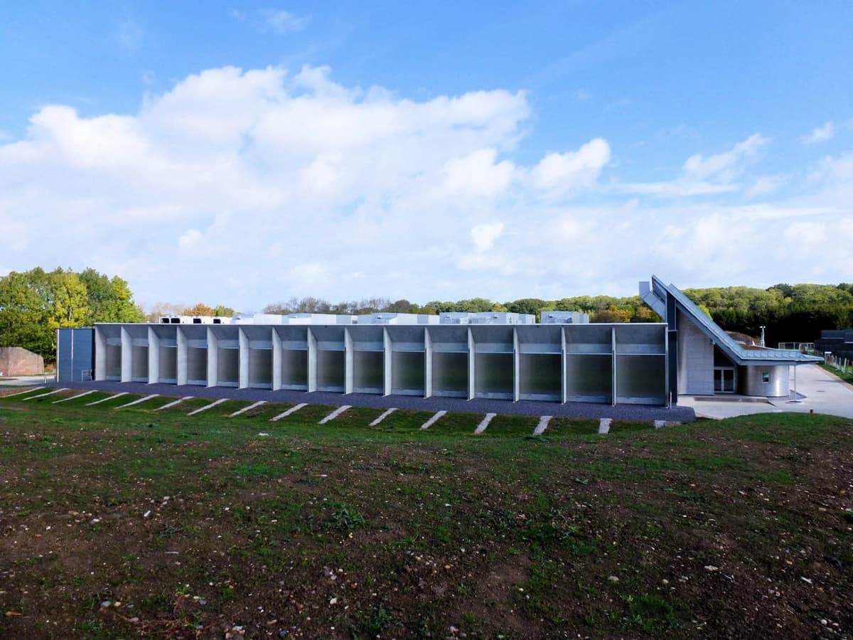Long grey-metal film store building with a sloping roof on grass under a blue sky with clouds.