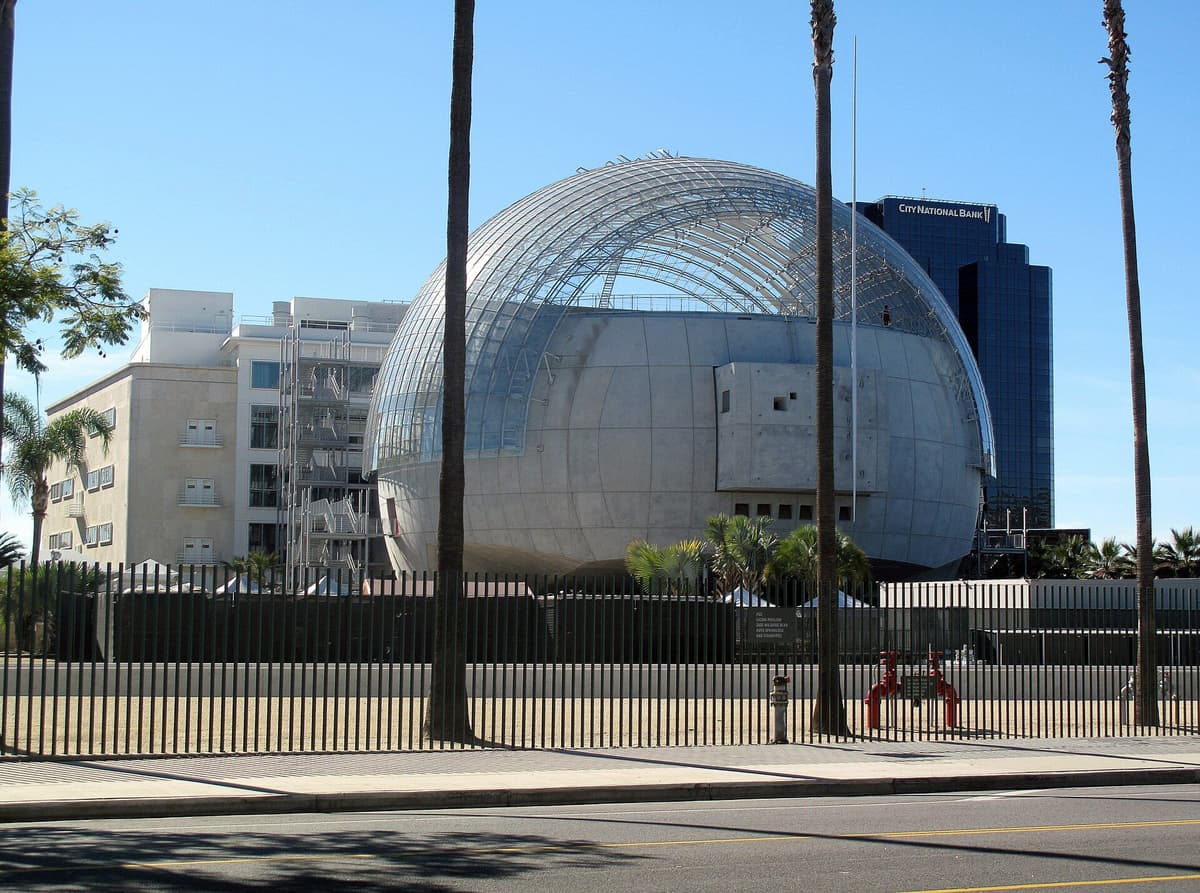 The spherical glass and metal Sphere building of the Academy Museum of Motion Pictures against a blue sky.