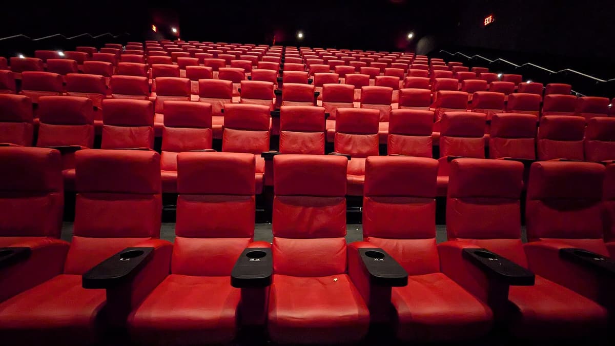 Rows of red cinema seats with armrests and cup holders in a dark auditorium, facing the screen