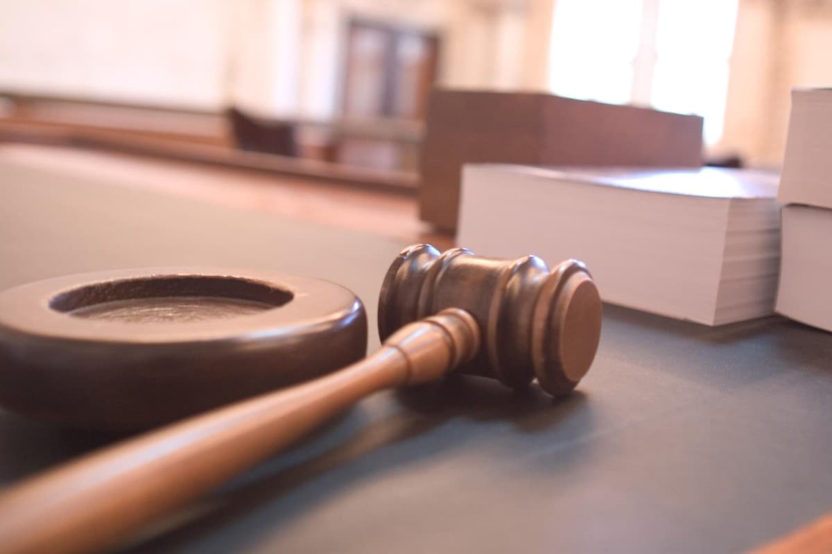 A wooden gavel and sound block resting on a courtroom desk beside stacks of law books