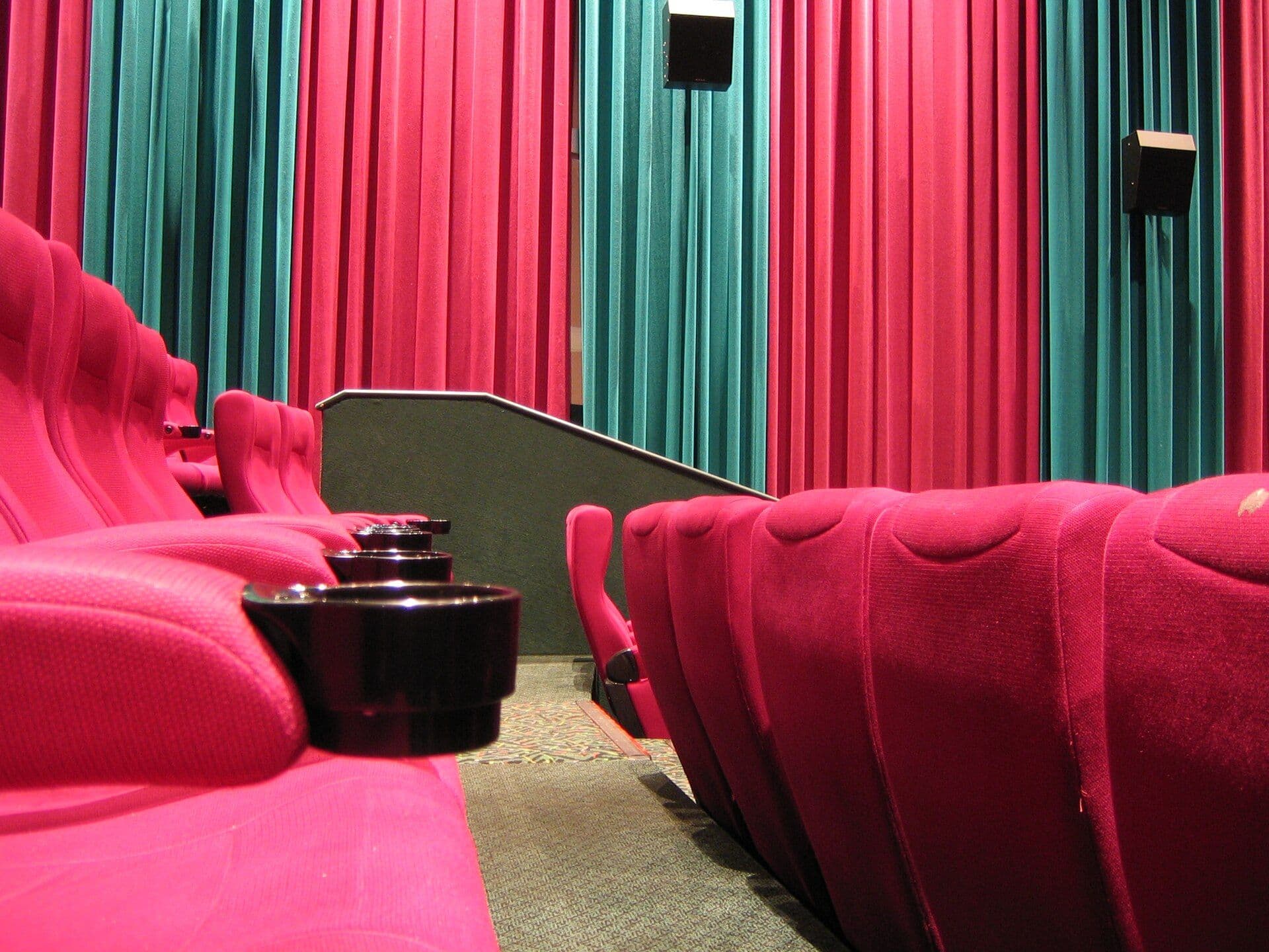 Interior of a modern movie theater with bright pink seats and teal acoustic wall panels